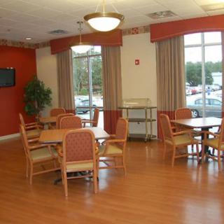 A spacious dining area with tables and chairs, featuring large windows and wooden flooring.