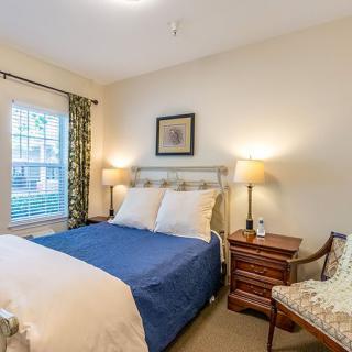 A cozy bedroom with a bed, nightstands with lamps, a window with curtains, and a decorative painting on the wall.