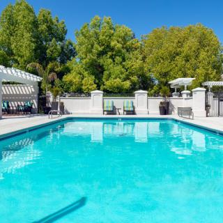 A serene outdoor swimming pool surrounded by trees under a clear blue sky.