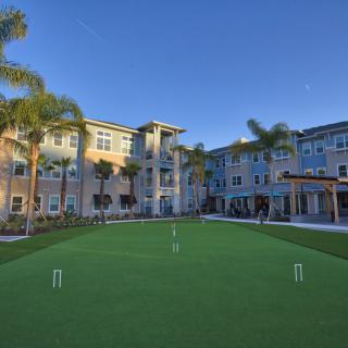 A sunny day at a residential apartment complex featuring a well-maintained croquet court and palm trees.