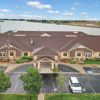 A scenic view of a building by the lake with a driveway and parking area.