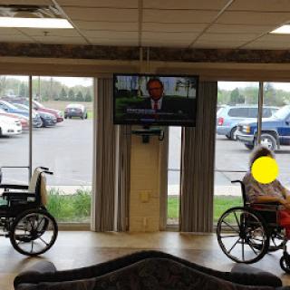 A serene waiting area with two individuals in wheelchairs, watching a news broadcast on the television.