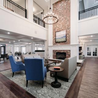 A spacious and elegantly designed living room featuring a high ceiling, modern decor, and a cozy seating area by the fireplace.