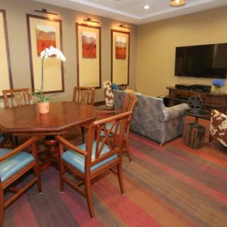 A cozy living room with a dining area, featuring a wooden table and chairs, a sofa, and a television.