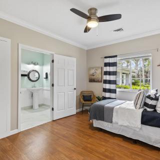 A modern bedroom with a ceiling fan, wooden flooring, and abundant natural light coming through a window with striped curtains.