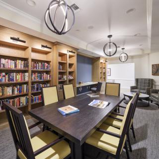 A modern library meeting room with bookshelves, a large table, and comfortable chairs.