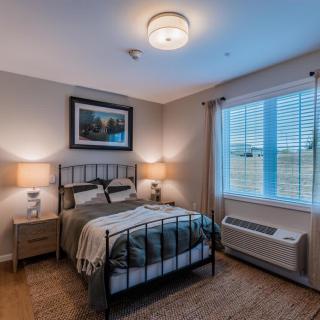 A cozy and modern bedroom with warm lighting, featuring a comfortable bed, two bedside lamps, and a window with blinds.