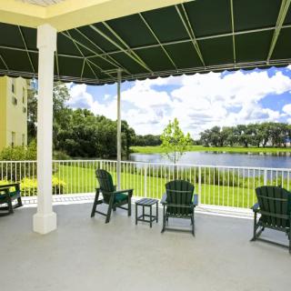 A covered patio with chairs overlooking a tranquil lake and greenery.