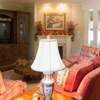 A cozy living room featuring a comfortable sofa, a central coffee table with a decorative lamp, and a classic wooden entertainment center with a television. The fireplace adds warmth and charm to the space.