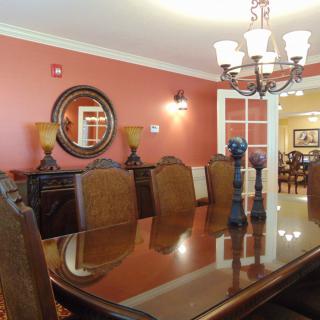 A stylish dining room with a large wooden table and ornate chairs, illuminated by an elegant chandelier.