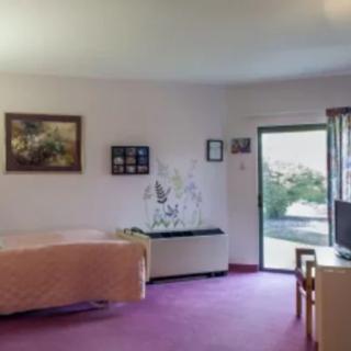 A cozy bedroom with purple flooring, decorated with paintings and a table near the window.
