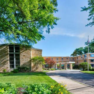 A sunny day view of a modern building with a driveway surrounded by lush greenery.