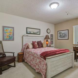A cozy bedroom with a decorated bed, artwork on the walls, and a window providing natural light.