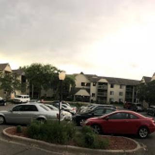 A view of an apartment complex with cars parked in the lot under a cloudy sky.
