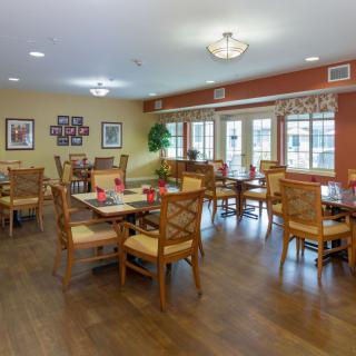 A spacious and well-lit dining room with multiple tables and chairs, featuring wooden flooring and stylish decor.