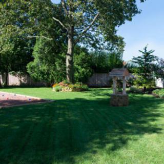 A tranquil garden with a well-manicured lawn, surrounded by trees and featuring a decorative well.