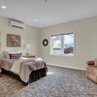 A cozy bedroom with a neatly made bed, art on the walls, and a comfortable armchair by the window.
