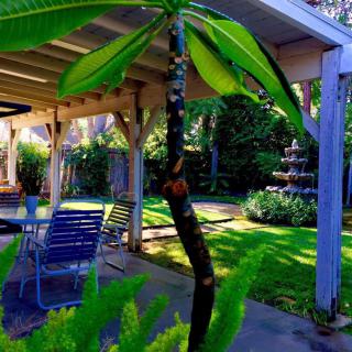 A serene backyard garden featuring a patio area with seating, lush greenery, and a decorative fountain.