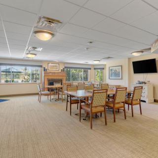 A spacious and well-lit dining area with tables, chairs, a television, and large windows.
