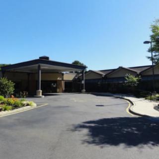 A view of a building entrance with a circular driveway and landscaping on a sunny day.