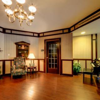 A cozy living room with elegant wood paneling, featuring a chandelier, armchair, and piano.