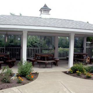 An outdoor gazebo surrounded by a garden with several picnic tables inside.