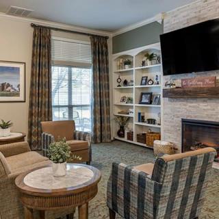A cozy living room with comfortable armchairs, a fireplace, and a television mounted above bookshelves.