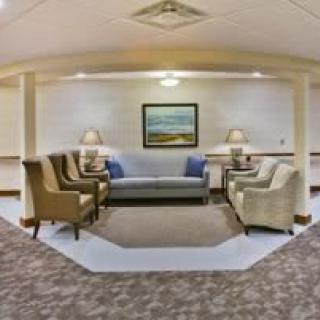 A cozy lobby seating area with sofas and armchairs arranged around a central rug, enhanced by soft lighting and wall art.