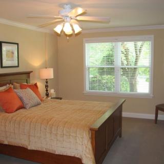 A cozy bedroom with a large bed, bedside lamp, and ceiling fan, filled with natural light from the window.