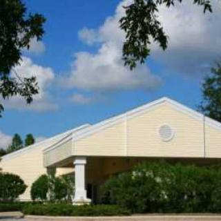 A church building with a bright, clear sky and surrounding greenery.