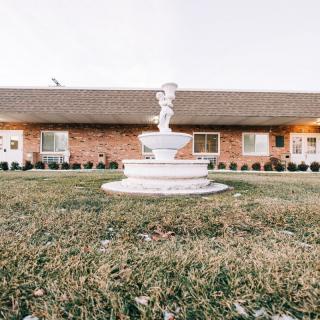 A picturesque garden scene featuring a white fountain in front of a brick building.
