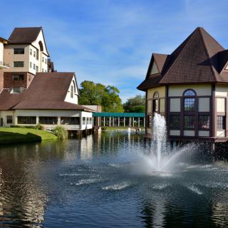 A scenic view of a resort with buildings by a lake and a fountain in the foreground.