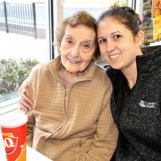 An elderly woman and a young woman smiling together indoors.