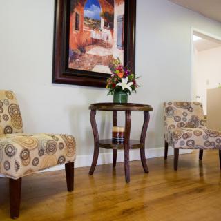 A cozy waiting area with patterned chairs and a small table adorned with flowers beneath a colorful painting.