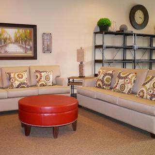 A modern living room setup with neutral-toned sofas, colorful cushions, a red round coffee table, and wall art.