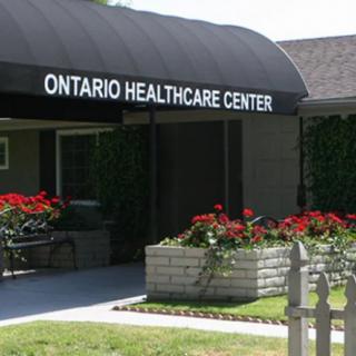 Entrance of the Ontario Healthcare Center with a black awning and decorative flower beds.