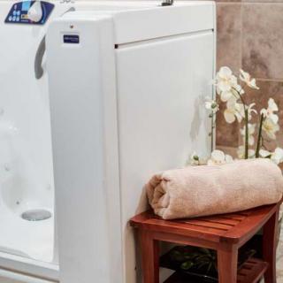 A walk-in bathtub accompanied by a wooden bench with a rolled-up towel and decorative flowers, creating a spa-like atmosphere.