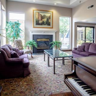 A cozy living room with plush sofas, a piano, and a fireplace, decorated with plants and artwork.