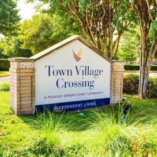Entrance sign for Town Village Crossing, surrounded by greenery.
