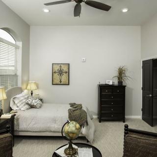 A cozy bedroom featuring a neatly made bed, a tall dresser, and modern decor with a ceiling fan overhead.