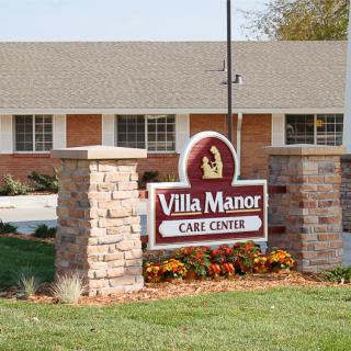 A sign for Villa Manor Care Center in front of a brick building.
