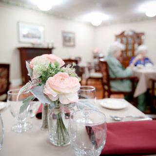 A cozy dining area for elderly residents, adorned with fresh flowers and set for a meal.