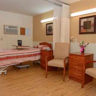 A clean and well-organized hospital room with a single bed, chairs, and a small table with flowers.