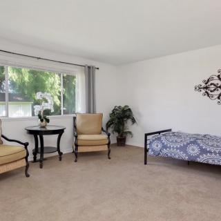 A cozy living space with two armchairs, a small round table, and a bed near a large window.