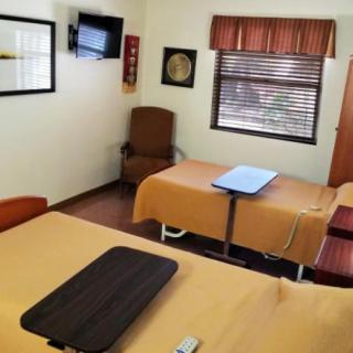 A hospital room with two patient beds, a wall-mounted television, and window blinds.