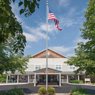 A building with an American flag flying in front, surrounded by trees under a blue sky.