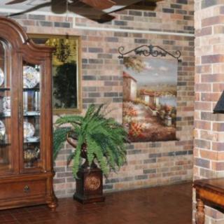 A cozy room with a brick wall, featuring a wooden china cabinet, a decorative plant, and various artworks.