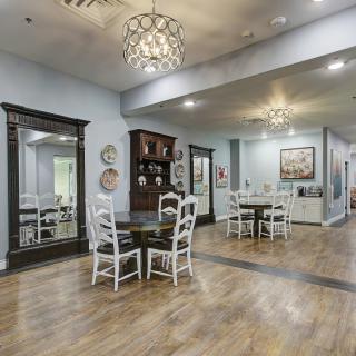 A spacious and well-lit dining area with wooden flooring, furnished with tables and chairs, adorned with elegant chandeliers.
