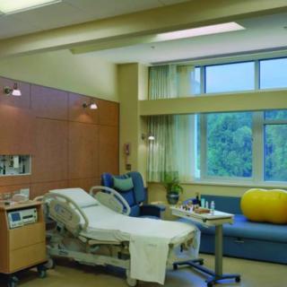 A modern hospital patient room with a bed, medical equipment, and a sofa by the window.