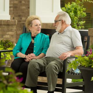 An elderly couple sitting on a bench having a conversation in a garden setting.